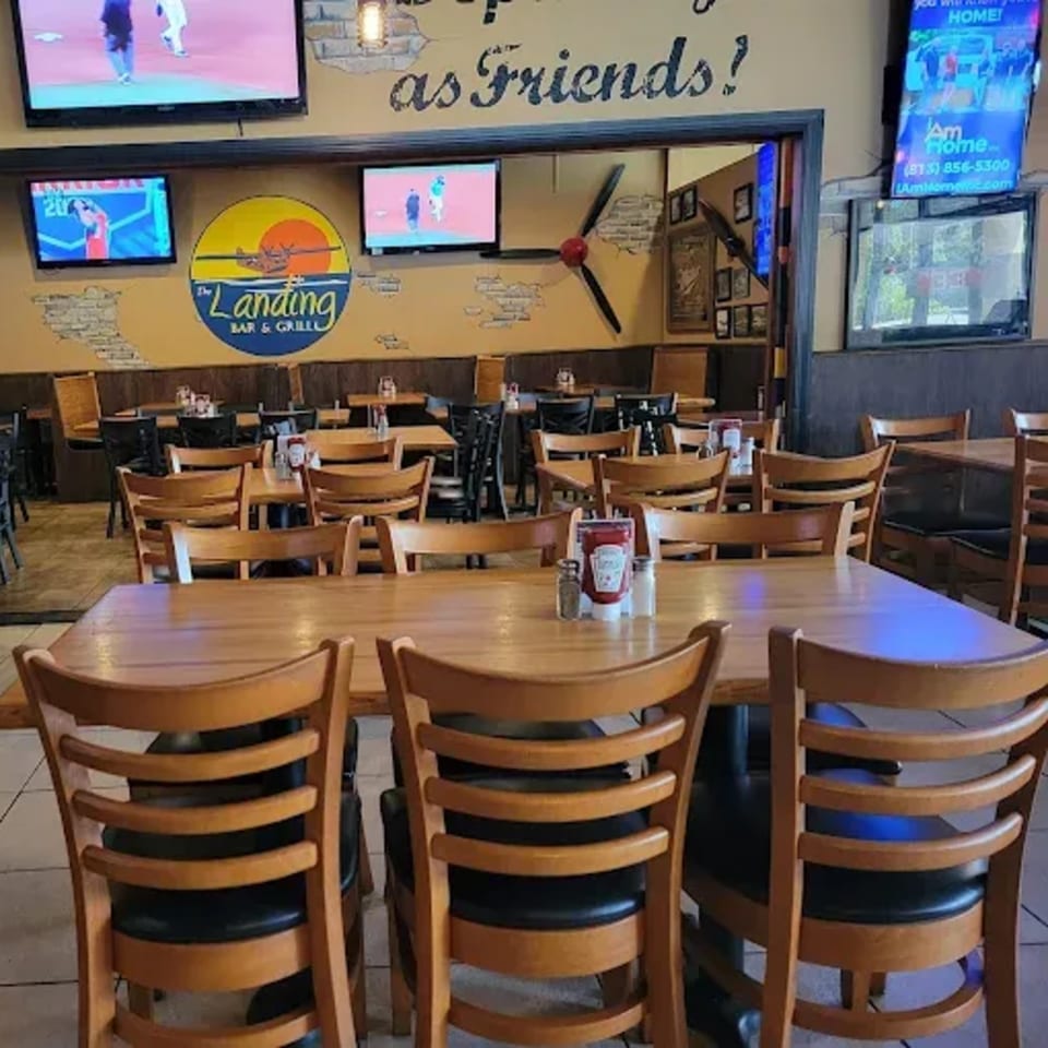 Interior of The Landing Bar and Grill with wooden tables and chairs, TVs, and a propeller decoration.