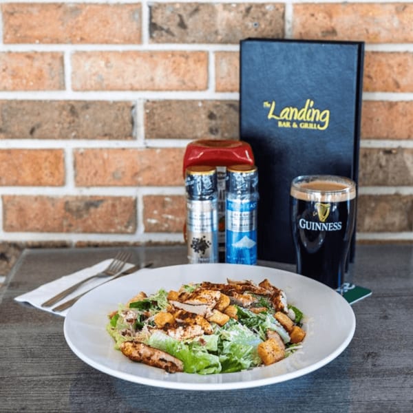 Grilled chicken Caesar salad, Guinness beer, and a menu from The Landing Bar & Grill.